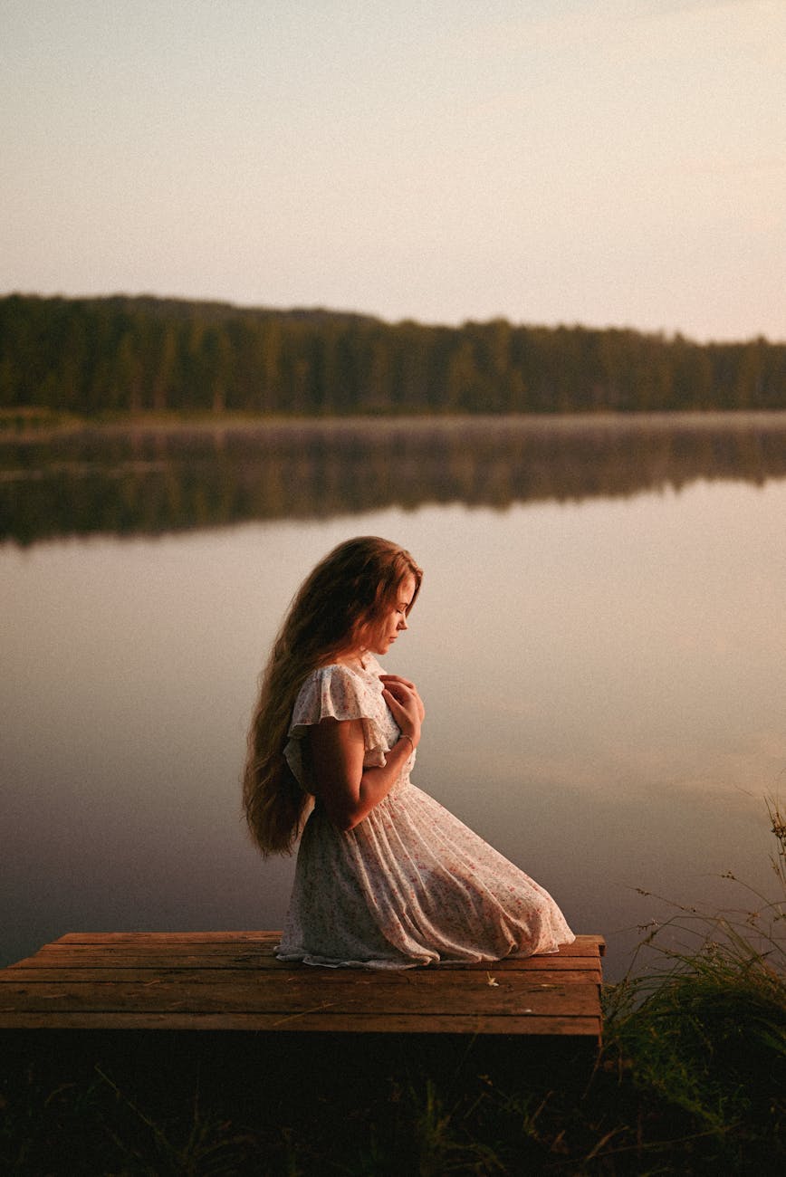 Woman practicing yoga on a wooden dock by the lake at sunset.